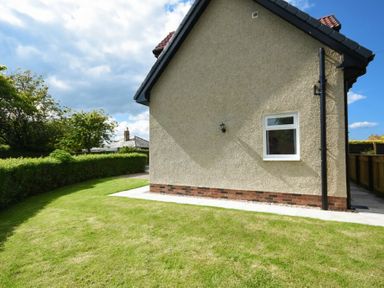 A side view of a house with a small window and a garden with green grass and a hedge at The Chevy in Seahouses