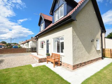 A house with a small garden and wooden bench outside at The Chevy in Seahouses