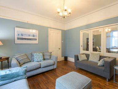 A living room with two sofas an ottoman wooden floor and blue walls at Nettie's View in Amble
