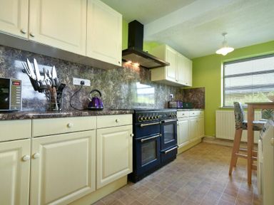 A kitchen with cream cabinets a black stove a microwave and a wooden table with chairs at Nettie's View in Amble