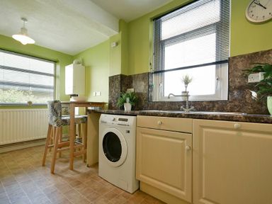 A kitchen with a washing machine under the counter and two chairs at a wooden dining table by the window at Nettie's View in Amble