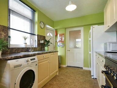 A kitchen with a washing machine cabinets countertops plants a fridge a microwave and a clock on the wall at Nettie's View in Amble
