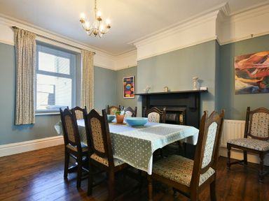 A dining room with a table covered in a polka dot tablecloth surrounded by eight wooden chairs and a black fireplace on the wall at Nettie's View in Amble