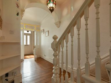 A hallway with wooden floor a staircase with white balusters and a front door with stained glass panels at Netties View in Amble