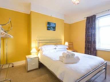 A bedroom with a double bed towels on the bed two bedside tables two lamps a chair a clothing rack and a window with curtains at Nettie's View in Amble