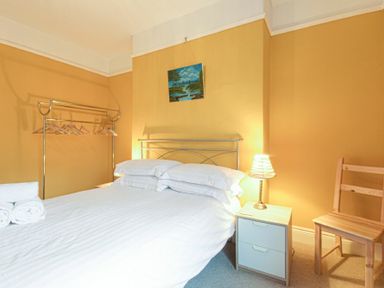 A bedroom with a bed bedside table with lamp wooden chair and clothes rack at Nettie's View in Amble