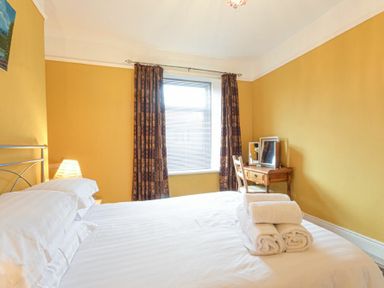 A bedroom with a double bed and towels on the bed a wooden desk with a mirror and chair by the window at Nettie's View in Amble