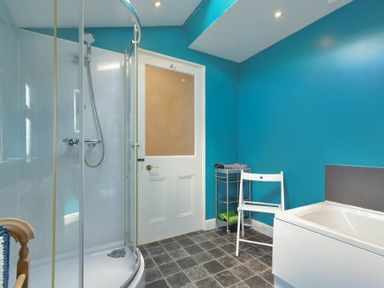 A bathroom with a curved glass shower enclosure a white bathtub a white chair and a storage rack at Nettie's View in Amble