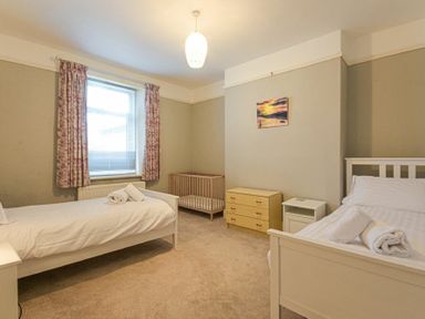 A bedroom with two single beds a crib a chest of drawers and a window with floral curtains at Netties View in Amble