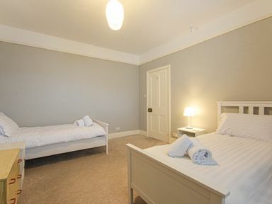 A bedroom with two single beds a bedside table with a lamp a wooden dresser and a closed door at Nettie's View in Amble