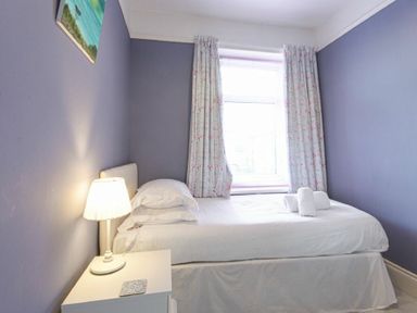 A bedroom with a bed a nightstand with a lamp and a window with curtains at Nettie's View in Amble