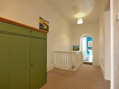 A hallway with striped carpet a green cabinet white railing and an arched doorway showing a bathroom at Nettie's View in Amble