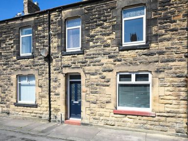 Stone exterior of a terraced house with a blue door and windows with blinds in Amble