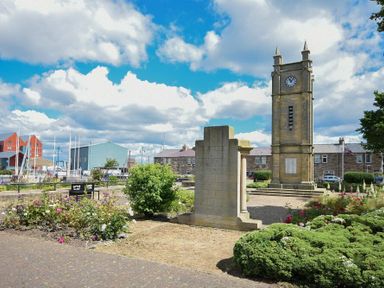 An outdoor park area with a clock tower rose bushes and buildings in Amble