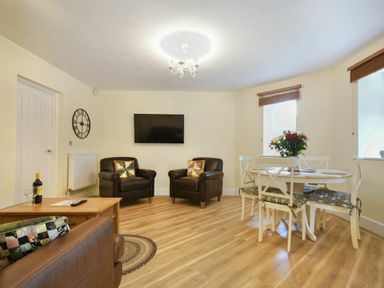 A living room with two brown armchairs a round dining table with four chairs and a mounted television at The Lodge (Alnwick) in Alnwick