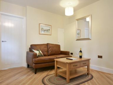 A living room with a brown leather sofa a wooden coffee table a bottle of wine a wine glass a framed picture and a wall mirror at The Lodge (Alnwick) in Alnwick