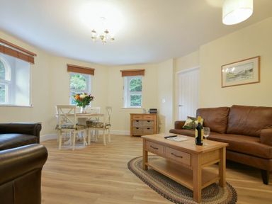 A living room with brown leather sofas a wooden coffee table a dining table with chairs and flowers at The Lodge (Alnwick) in Alnwick