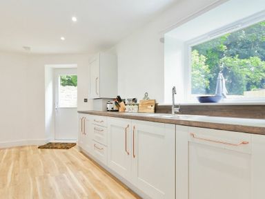 A kitchen with white cabinets wooden countertops a sink and a large window at The Lodge Alnwick