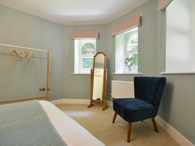 A bedroom corner with a blue chair a freestanding mirror a clothes rack with hangers and two windows at The Lodge Alnwick