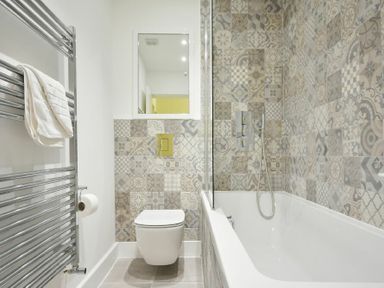 A bathroom with a bathtub shower combination and patterned tiled walls at The Lodge Alnwick