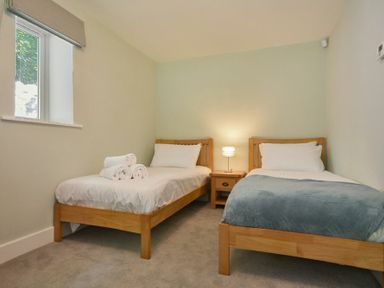 A bedroom with two single wooden beds and a nightstand with a lamp in between at The Lodge (Alnwick) in Alnwick
