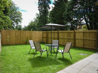 A fenced backyard with a round table umbrella and four chairs on grass at The Lodge (Alnwick) in Alnwick