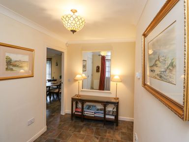 A hallway with a console table holding books and two lamps a large mirror above and framed paintings on the walls at Rokeby Bamburgh