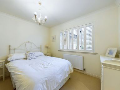 A bedroom with a bed bedside tables a lamp a window with shutters and a dresser at Rokeby in Bamburgh