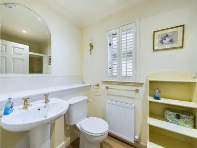 A bathroom with a pedestal sink and toilet beside a window and a shelving unit at Rokeby in Bamburgh