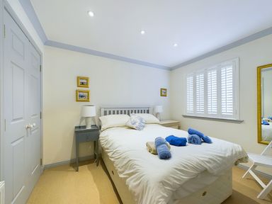 A bedroom with a double bed with white bedding blue and beige towels on top two bedside tables with lamps a window with white shutters a mirror on the wall and a wardrobe Rokeby Bamburgh