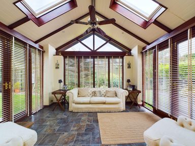 A sunroom with beige sofas a ceiling fan wooden blinds and tiled floor at Rokeby in Bamburgh