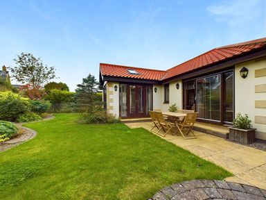 A backyard with grass patio dining table and chairs outside a house with red roof at Rokeby Bamburgh