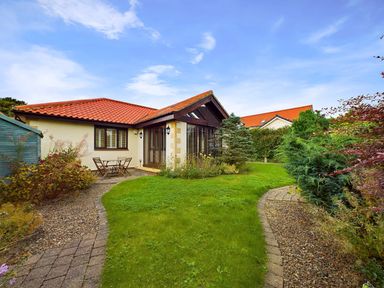 A garden with a lawn path shrubs small table and chairs next to a house with a red tiled roof at Rokeby in Bamburgh