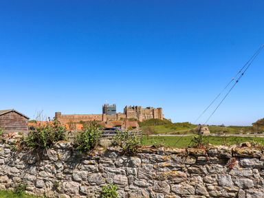A castle view with a stone wall and shed at Dunford Cottage Bamburgh