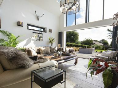A living room with sofas cushions a coffee table and large windows opening to a garden at Marmalade Cottage in Seahouses