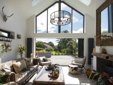 A living room with large windows open to a garden a leather sofa armchairs a coffee table and a fireplace at Marmalade Cottage in Seahouses