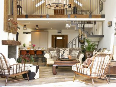 A living room with two armchairs and a sofa around a wooden coffee table with a staircase and kitchen in the background at Marmalade Cottage in Seahouses
