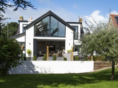 A two-story house with large triangular windows and an outdoor seating area at Marmalade Cottage in Seahouses
