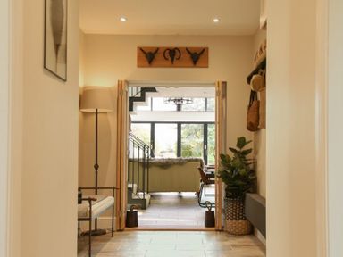 A hallway with a bench a floor lamp plants and decorative wall hooks leading to a living room at Marmalade Cottage in Seahouses