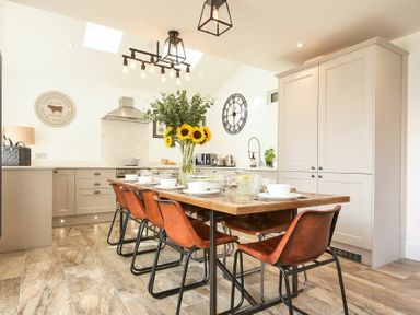 A kitchen with a wooden dining table and orange chairs and a vase of sunflowers at Marmalade Cottage in Seahouses