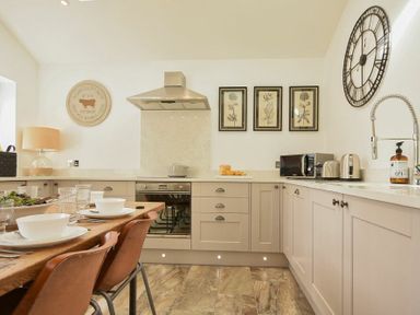 A kitchen with beige cabinets a wooden dining table with chairs and kitchen appliances at Marmalade Cottage in Seahouses