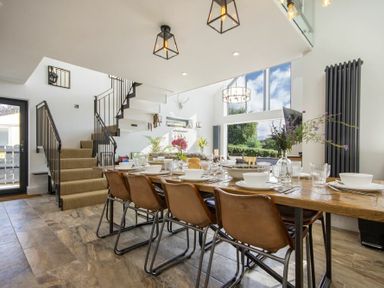 A dining area with a wooden table set with dishes and brown chairs next to stairs at Marmalade Cottage in Seahouses