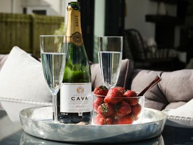 A bottle of cava brut with two glasses of water and a bowl of strawberries on a tray on a table in a living room at Marmalade Cottage in Seahouses