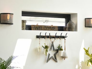 A wall with a welcome sign on a window ledge and hooks holding decorative items at Marmalade Cottage in Seahouses
