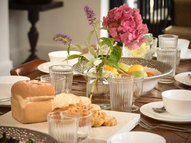 A dining table with glasses bowls cutlery bread fruit and flowers at Marmalade Cottage in Seahouses