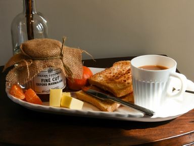 A breakfast plate with toast, cheese, orange slices, a jar of marmalade, and a cup of tea at Marmalade Cottage in Seahouses