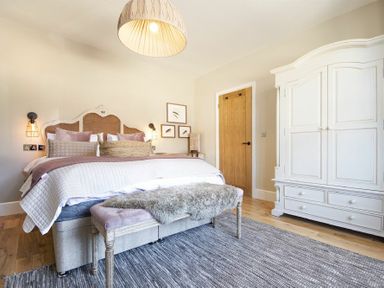 A bedroom with a bed with pillows and blankets a bench with a fur throw a wooden door and a white wardrobe at Marmalade Cottage in Seahouses