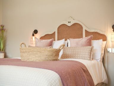 A bedroom with a bed with a carved headboard pillows a pink throw and a wicker basket at Marmalade Cottage in Seahouses
