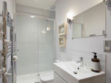 A bathroom with a shower enclosure sink with faucet mirror and wall decorations at Marmalade Cottage in Seahouses