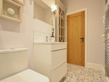 A bathroom with a toilet vanity cabinet a mirror towel rail and wooden door at Marmalade Cottage in Seahouses
